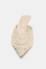Zapato mule destalonado color crudo, con tacón fino alto, punta fina y cuerpo con bordados texturizados y apliques de cuentas.