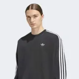 Buzo Adidas de cuello redondo con corte oversize, confeccionado en tejido de punto. Presenta las icónicas tres franjas blancas en las mangas y el logo del trifolio bordado en el pecho.