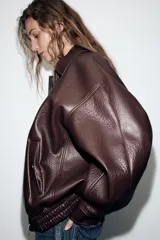 Cazadora estilo bomber de efecto piel en color bordó, con cuello solapa, manga larga, bolsillos delanteros de vivo con botón a presión y bajo elástico. Cierre frontal con cremallera oculta y botones a presión.