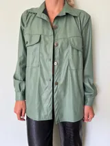Camisa verde de cuero sintético con cuello clásico, cierre frontal con botones metálicos y dos bolsillos con solapa en el pecho.