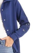 Campera liviana de modal con cuello solapa y cierre frontal mediante broches metálicos. Presenta mangas largas con detalles de bordado floral calado y puños en rib, además de bolsillos laterales funcionales.