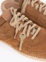Slide estilo alpargata confeccionado en cuero descarne color celeste, con cordones beige, detalles de flecos y dijes colgantes, sobre una base de yute trenzado.