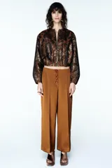 Chaqueta estilo bomber de cuello redondo y manga larga, confeccionada en tejido jacquard con acabado metalizado brillante. Presenta diseño con pliegues y cierre frontal con cremallera.
