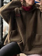 Campera tipo hoodie confeccionada en tela sherpa color verde oliva, con diseño de apliques bordados en la espalda que representan una flor y una fruta. Presenta capucha integrada y corte holgado.