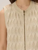 Chaleco de punto color beige con cierre frontal y patrón de rombos texturizados, sin mangas y con cuello redondo.