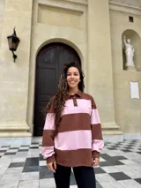 Buzo deportivo de corte holgado con diseño de rayas horizontales anchas en color marrón y rosado. Presenta cuello tipo polo con cierre frontal de botones y mangas largas con puños ajustados.
