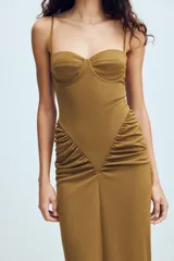 Vestido largo color tostado con diseño estilo corsé, escote corazón con aros y tirantes finos. Presenta un corte ajustado en la cintura con detalle de frunces laterales que aportan volumen a la falda.