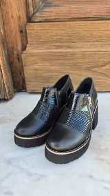 Zapatos de tacón alto y plataforma con diseño de caña baja, confeccionados en combinación de cuero liso, charol y detalles con textura animal print. Presentan cierre lateral de cremallera y suela gruesa con costuras visibles.