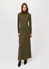 Vestido largo de punto en color verde oliva, con cuello alto y manga larga. Presenta un diseño ajustado en la parte superior que se extiende hacia una falda recta, con un detalle metálico decorativo en el lateral de la cintura.
