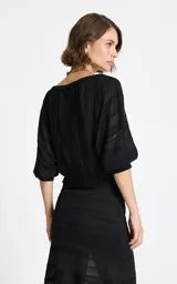 Blusa negra de encaje con hombros caídos, mangas tres cuartos con puños ajustados y diseño de paneles verticales texturizados.