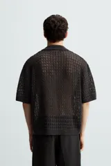 Polo de manga corta confeccionado en tejido de punto calado con estructura abierta. Presenta un diseño de corte relajado, cuello solapa con abertura frontal en pico y terminaciones acanaladas en puños y bajo.