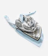 Pañuelo rectangular de satén con estampado paisley en tonos blanco, azul claro y beige. El pañuelo se anuda bajo la barbilla, cubriendo la cabeza.