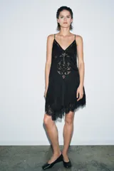 Top negro de tirantes finos con escote pico. Presenta bordados ornamentales en el frente y detalles de puntilla en el escote y el bajo asimétrico.