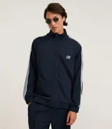 Campera deportiva de cuello alto con cierre frontal completo, mangas largas con rayas laterales blancas contrastantes y bolsillos laterales. Presenta un bordado pequeño en el pecho.