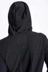 Campera deportiva de color negro con cierre frontal, capucha y mangas largas con puños elásticos. Presenta una textura ligera y un corte ajustado al cuerpo.