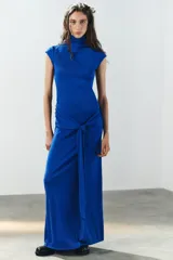 Vestido largo color azul, confeccionado en tejido elástico, con cuello alto, manga muy corta y detalle de lazada en la cintura. Cuenta con abertura en la espalda.