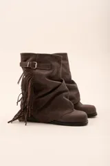 Botas de caña media color marrón chocolate, confeccionadas en cuero. Presentan un diseño arrugado en el empeine, una correa con hebilla metálica y flecos laterales.