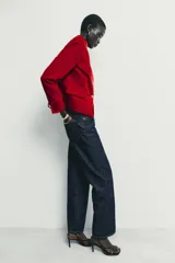 Blazer de terciopelo color rojo, con cuello subido, manga larga y cierre frontal cruzado con botones dorados. Presenta bolsillos delanteros con solapa.