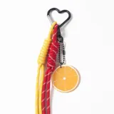 Llavero con mosquetón en forma de corazón, compuesto por dos cuerdas de paracaidista anudadas en colores amarillo y rojo, y un dije circular con diseño de rodaja de naranja.