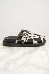 Zueco con capellada de cuero con estampado de vaca en blanco y negro, hebilla metálica plateada ajustable y suela track negra.