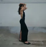 Vestido largo negro de corte ajustado, con espalda descubierta y detalle de tachas metálicas en los laterales. Presenta un tajo lateral en la falda.