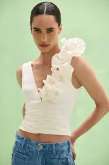 Top off white con escote en V y diseño drapeado en el torso. Cuenta con tiras anchas, destacándose una de ellas por estar decorada con apliques de flores volumétricas de tela.