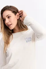 Remera de manga larga color verde oliva, con cuello redondo y estampa gráfica pequeña en el pecho con texto y dibujos lineales.