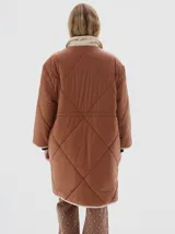 Tapado largo hasta las rodillas, color marrón, con vivos en color crema y cuello de pana. Tiene bolsillos delanteros, cierre frontal con botones a presión y cordón en la cintura para ajustar.