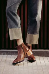 Botín de cuero negro, caña corta, con punta cuadrada y cierre lateral. Presenta un tacón de madera de altura media y detalles en charol con textura de cocodrilo en el talón.