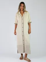 Vestido midi de punto color beige, con cuello solapa, mangas cortas y cierre frontal con botones. Presenta detalles de costuras y terminaciones en color mostaza, además de un diseño calado en el sector inferior de la falda.