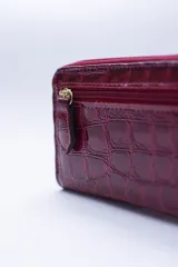 Billetera chica de cuero negro con textura tipo cocodrilo, cierre exterior, bolsillo para monedas con cierre en la parte trasera, múltiples ranuras para tarjetas y billetes, y forro rojo.