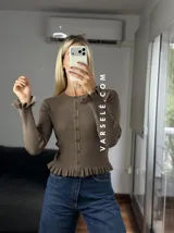 Saquito de tejido bremer color crema, con cuello redondo, cierre frontal de botones y detalles de volados en el ruedo y los puños.