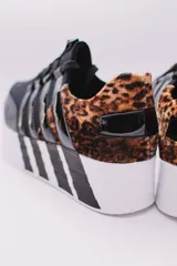 Zapatillas urbanas negras con plataforma blanca y detalles a rayas en el talón y la suela. Presentan un diseño con múltiples tiras elásticas en el empeine y puntera charolada.