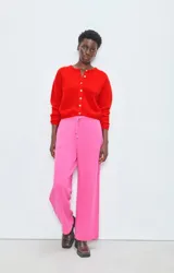 Cárdigan de punto rojo con cuello redondo, cierre frontal de botones y mangas largas con puños ajustados. Presenta un diseño de corte holgado y textura esponjosa.