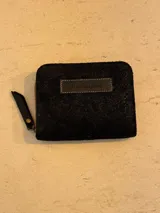 Billetera de cuero de pelo negro con cierre perimetral y etiqueta de marca cosida en el frente.