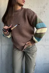 Sweater de tejido de punto con cuerpo en color marrón y mangas con diseño de rayas horizontales en tonos verde, turquesa y crema. Presenta cuello redondo y puños acanalados.