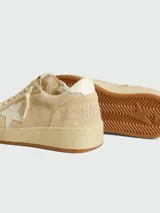Zapatillas deportivas Golden Goose modelo Ball Star, color beige claro, con estrella lateral en color crema y suela de goma color caramelo. Presentan un aspecto desgastado intencional y texto grabado en el lateral.