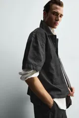 Camisa de manga corta con cuello solapa y cierre frontal de botones. Confeccionada en tejido denim de algodón, de corte relajado y aberturas laterales en el bajo.