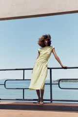Vestido midi confeccionado en hilatura de algodón de color amarillo, con cuello redondo, manga corta y detalles de frunces laterales ajustables con cordones. Presenta bajo asimétrico con acabado en línea evasé.