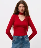 Blusa entallada de microfibra color blanco, con escote en V, mangas largas y detalle de frunces en los laterales. Presenta un lazo integrado en el cuello que permite anudarlo, aportando un toque sofisticado al diseño.