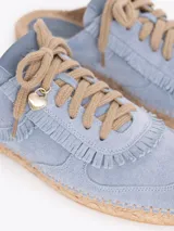 Slide estilo alpargata confeccionado en cuero descarne color celeste, con cordones beige, detalles de flecos y dijes colgantes, sobre una base de yute trenzado.
