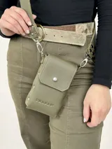 Bandolera porta celular de cuero genuino color verde militar, con textura granulada y logo "CHABAS" grabado en el frente. Cuenta con solapa con broche a presión y correa ajustable con remaches y argolla metálica.
