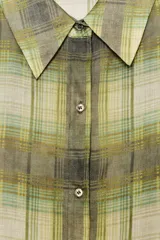 Camisa de manga larga con cuello solapa y cierre frontal de botones. Presenta un estampado de cuadros en tonos verdes, amarillos y grises, con un efecto ligeramente desvanecido o transparente.