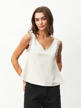 Blusa sin mangas color blanco off-white, con escote en V y detalles de encaje en los tirantes. Diseño holgado y fluido.