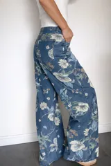Pantalón de jean corte wide leg con estampado floral en tonos azules, verdes y blancos. Presenta tiro alto, diseño de pierna amplia y bolsillos traseros.