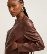 Campera básica de cuero sintético (PU) color marrón oscuro, con cuello redondo, cierre frontal y recortes decorativos. Cuenta con mangas largas y bolsillos con cierre.