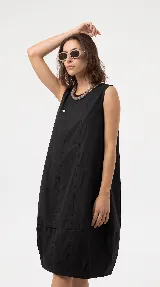 Vestido midi negro sin mangas, de corte amplio y relajado con silueta evasé y falda con volumen tipo globo. Presenta escote redondo, costuras verticales decorativas en el frente y un pequeño detalle de aplique metálico en el pecho.