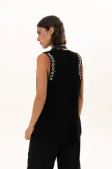 Chaleco negro de cuero descarne con silueta relajada y detalles de ojalillos metálicos plateados distribuidos en los bordes y sisas.