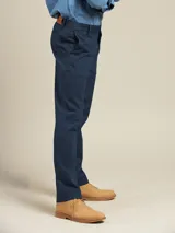 Pantalón de vestir color beige, de corte recto, con bolsillos laterales y traseros. Se ajusta a la cintura con cinturón de cuero marrón.