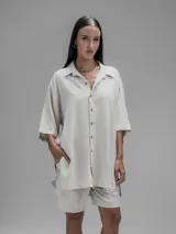 Camisa de corte oversize en color beige, confeccionada en tejido de lino y algodón. Presenta cuello clásico, cierre frontal con botones y mangas cortas amplias.